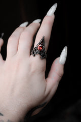 Hand wearing a decorative ring with a red gemstone against a dark background