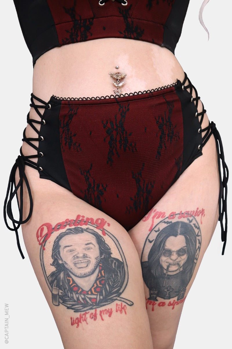 gothic woman wearing a black and red swimsuit with tattoos on their legs.