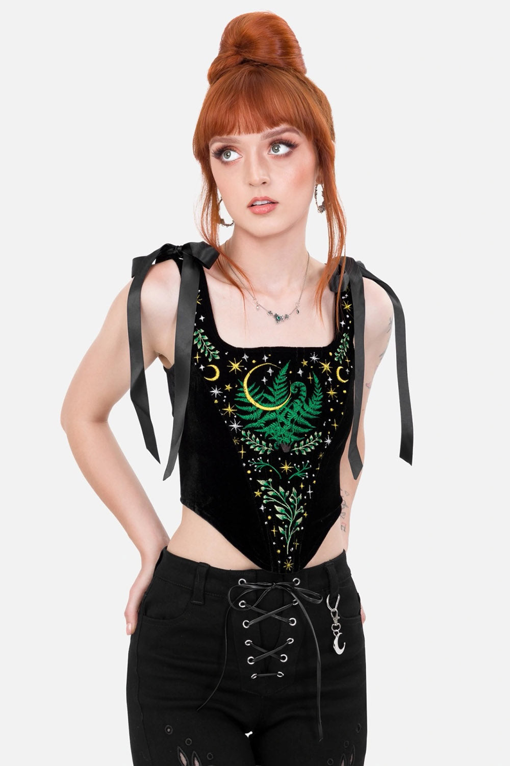 Woman wearing a black sleeveless corset top with green embroidery and black pants on a white background