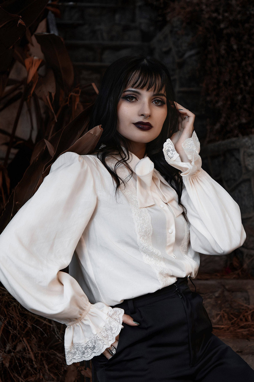 Woman wearing a white victorian blouse with lace details against a dark background