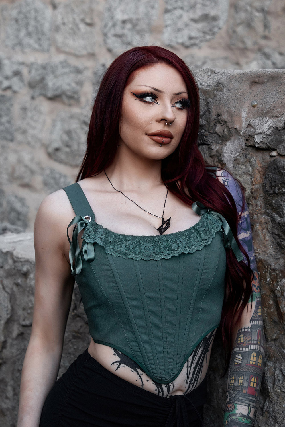 Woman wearing a green corset against a stone wall