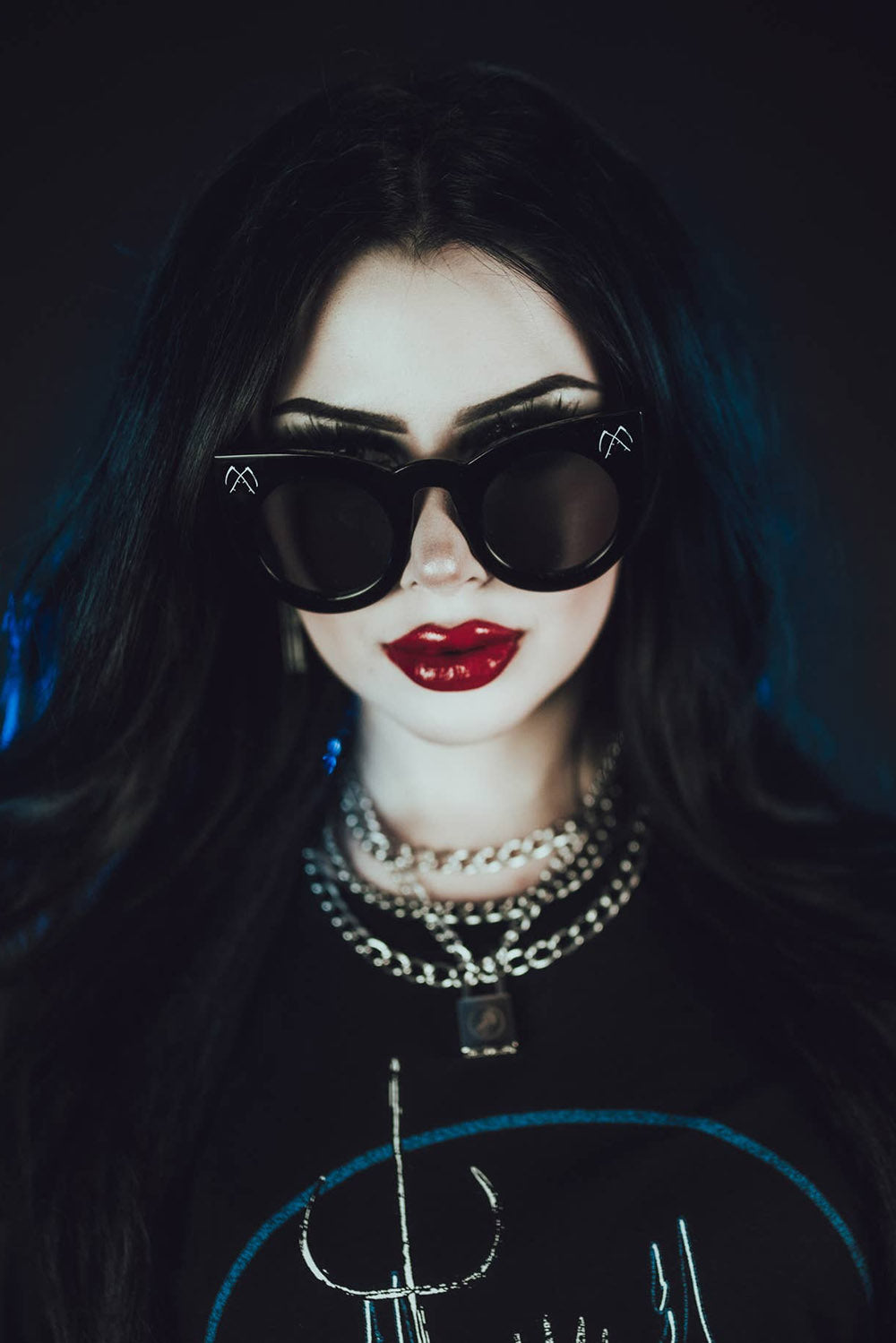 Person with dark hair and sunglasses wearing a black outfit with blue accents.
