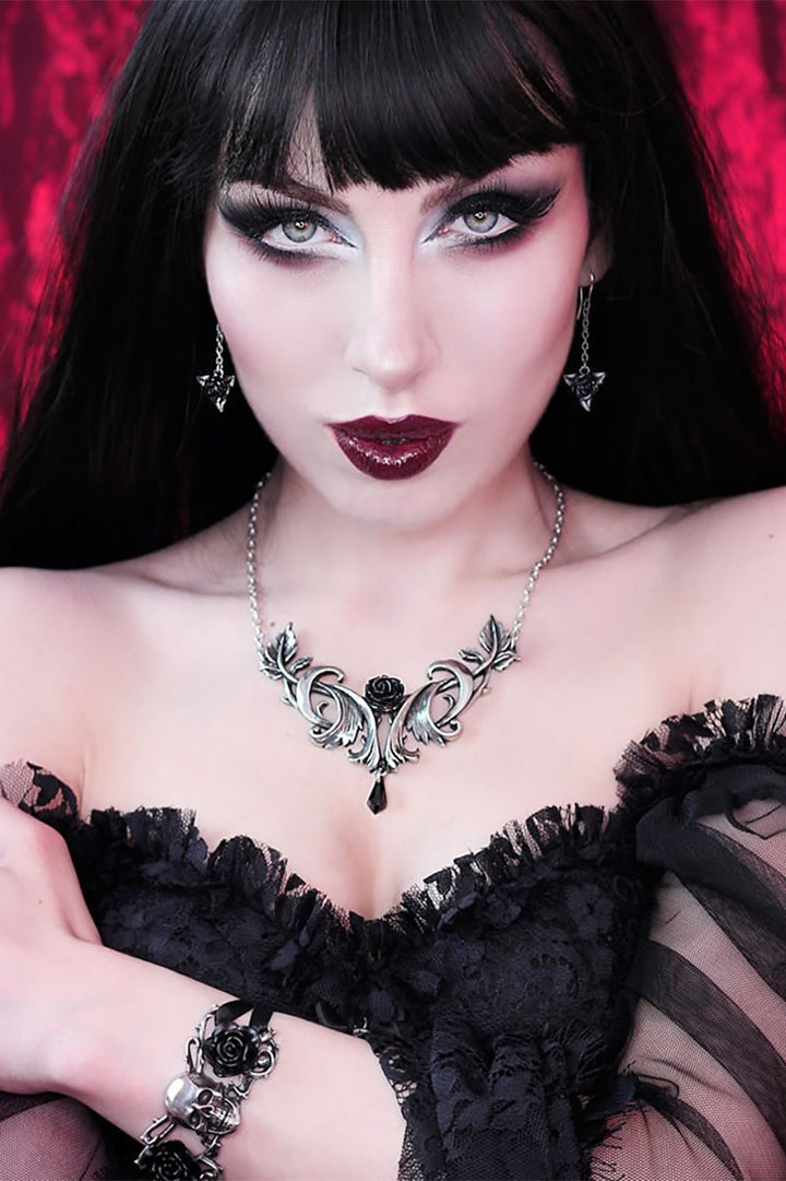 Woman in a black lace outfit with dark makeup and goth jewelry against a red background