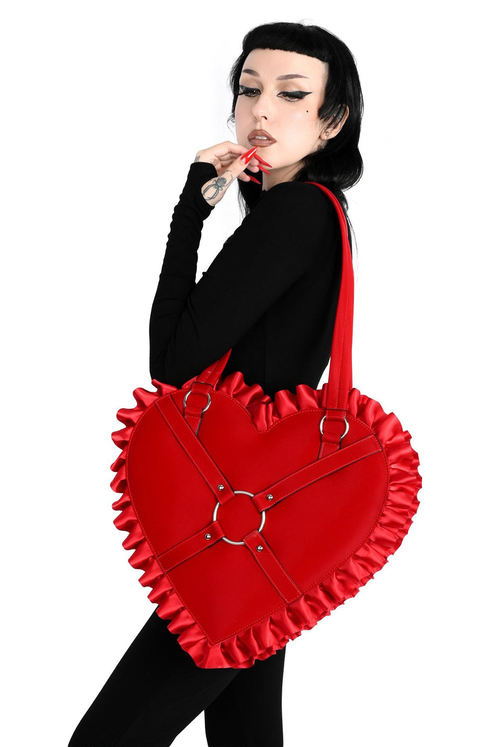 Person holding a red heart-shaped bag with ruffles and metal rings on a white background