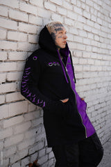 Person wearing a black and purple jacket leaning against a white brick wall.