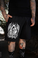 tattooed Person wearing black goth shorts with a white graphic design, standing outdoors.