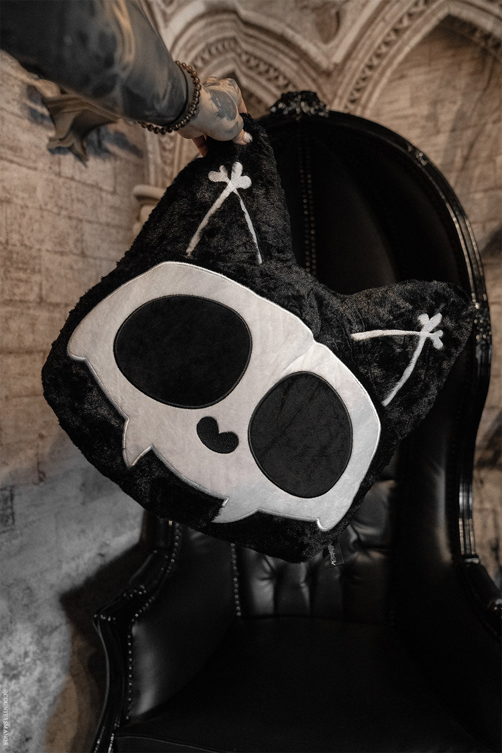 Black plush cat pillow with skull design on a dark background