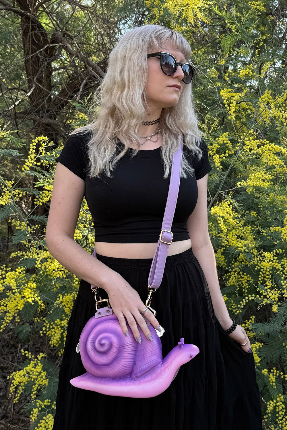 Person holding a purple snail-shaped handbag in front of yellow flowers