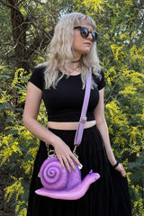Person holding a purple snail-shaped handbag in front of yellow flowers