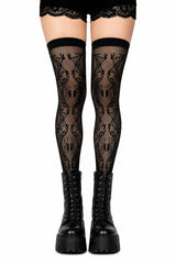 Black lace thigh-high stockings with a repeating spider pattern, worn with black lace-up platform boots against a white background.