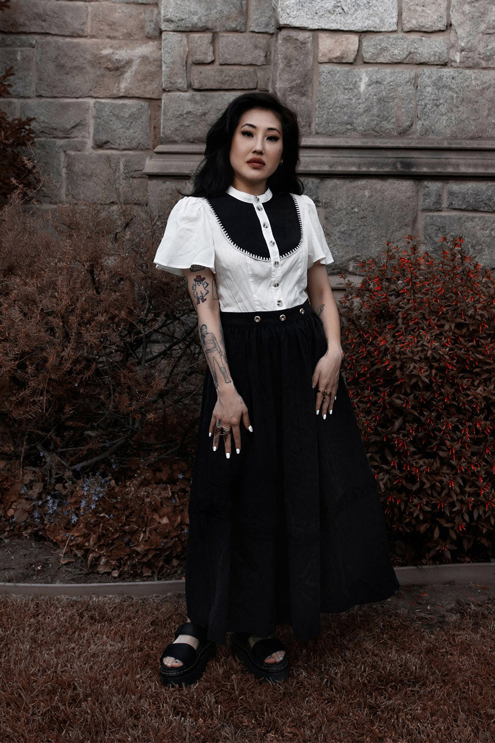 Woman in a white and black dress standing against a stone wall.