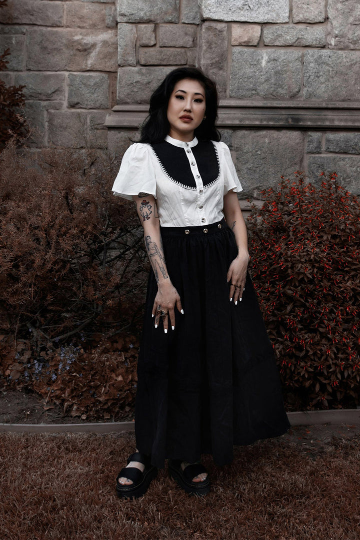 Woman in a white and black dress standing against a stone wall.