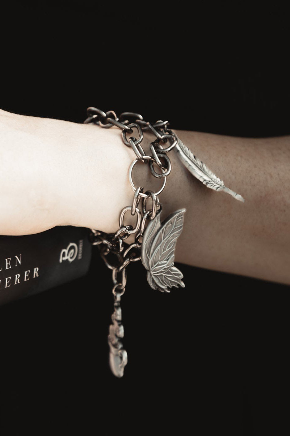 Bracelet with chain and butterfly moth charms on a wrist against a black background