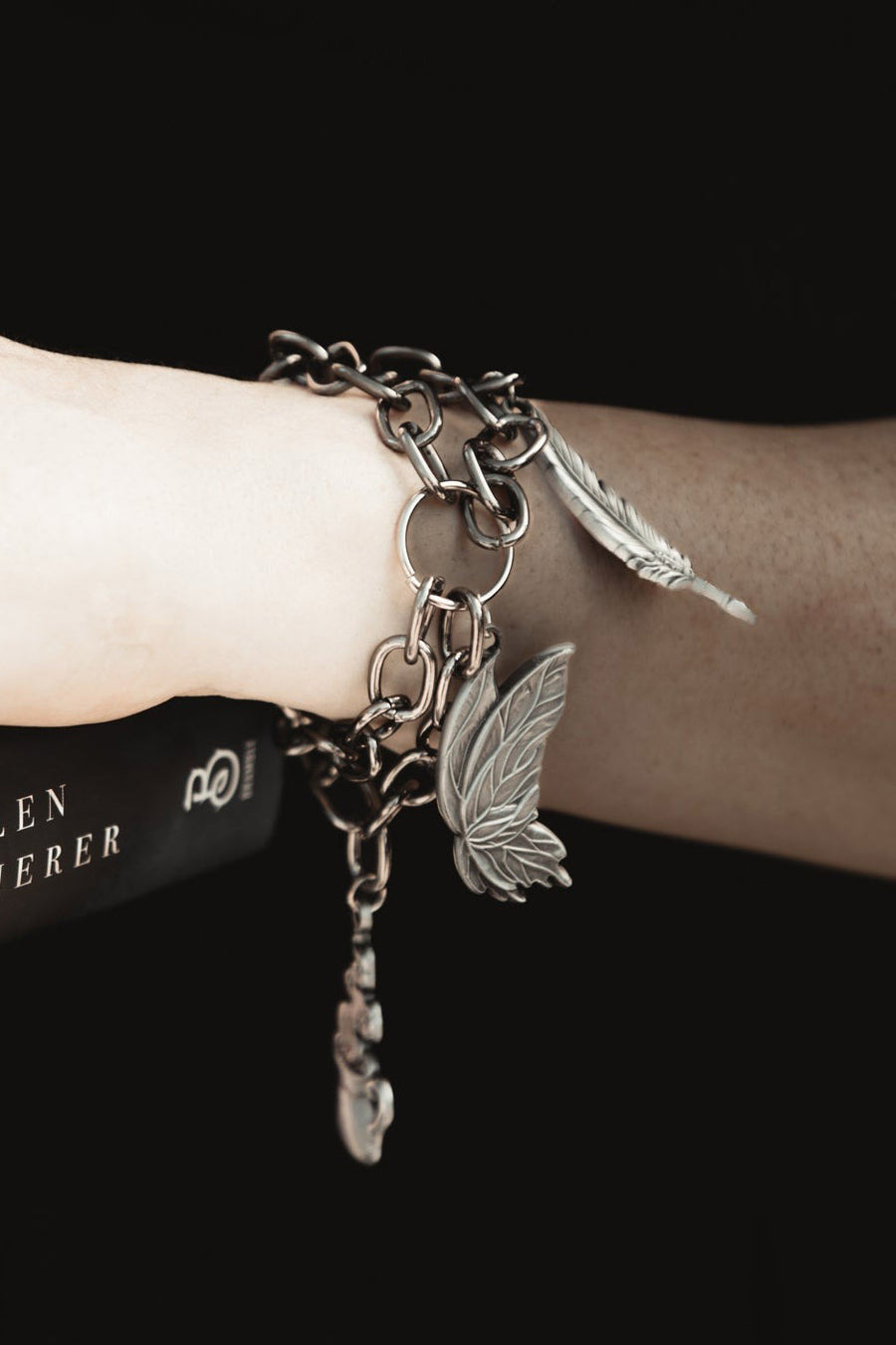 Bracelet with chain and butterfly moth charms on a wrist against a black background
