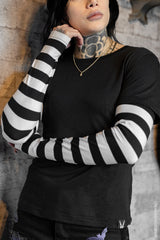 Person wearing a black short-sleeve shirt with black and white striped sleeves against a textured wall.