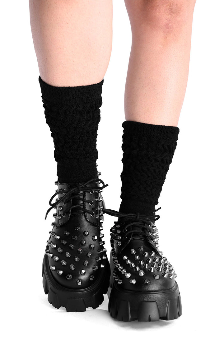 Black spiked platform shoes with black socks on a white background