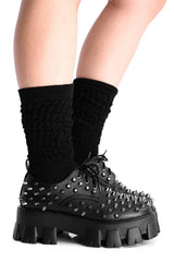 Black spiked platform shoes worn with black socks on a white background