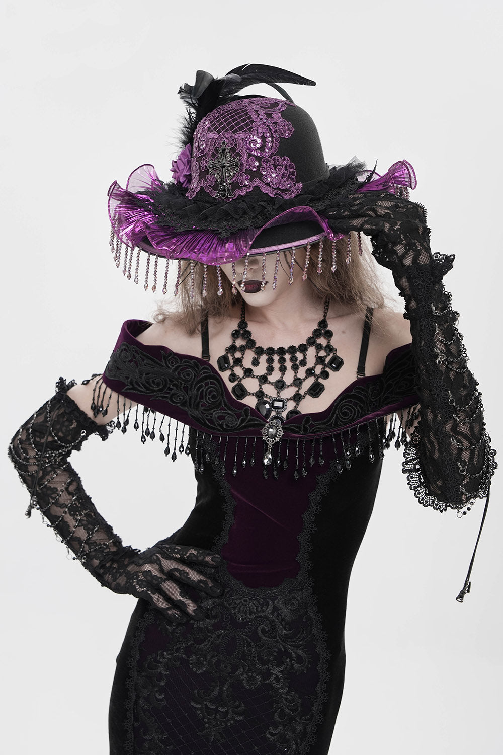 Person wearing a black and purple gothic outfit with a hat and gloves on a white background