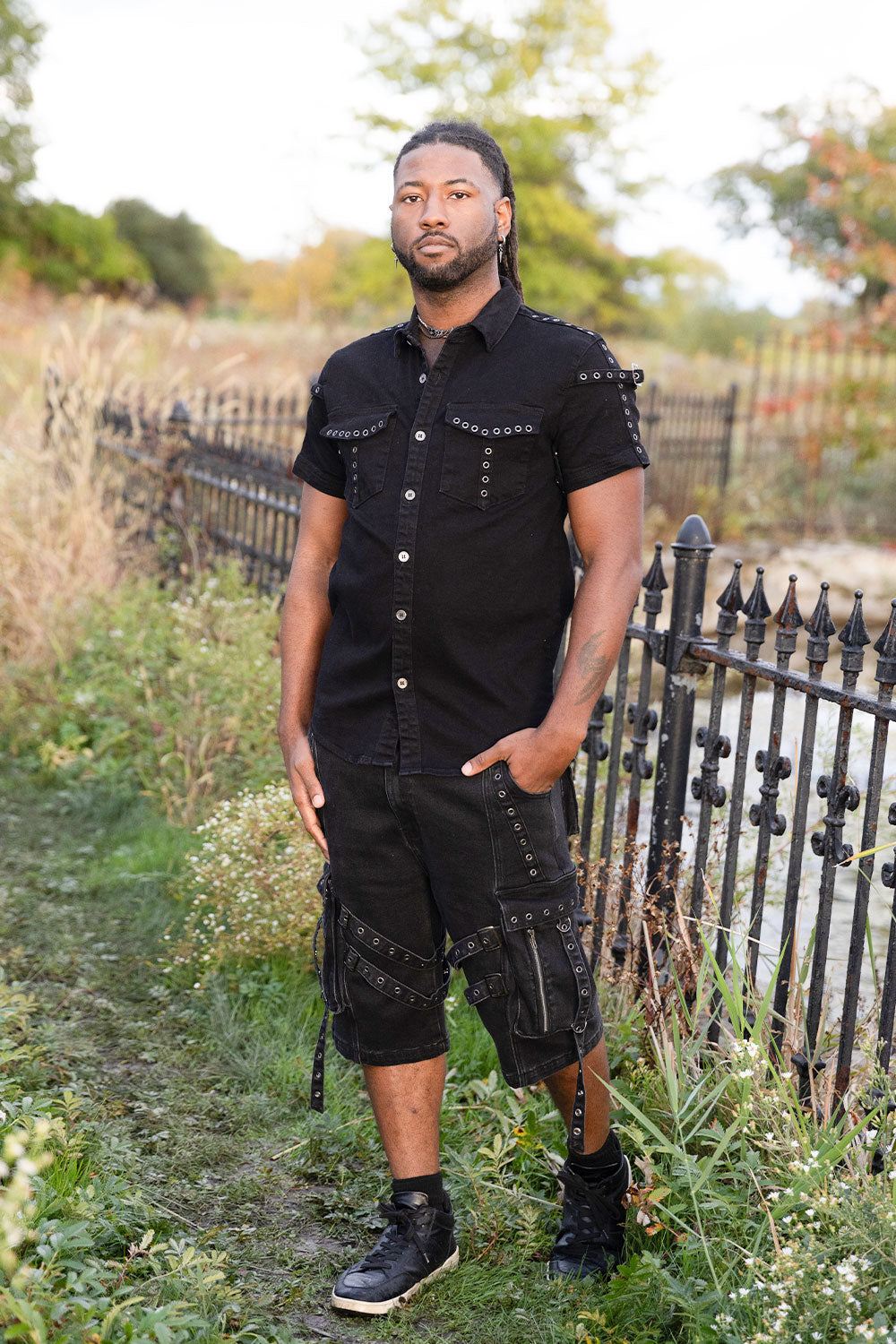 Mens black alternative fashion shirt with metal buckle shoulder details and functional front pockets for goth punk and edgy streetwear outfits