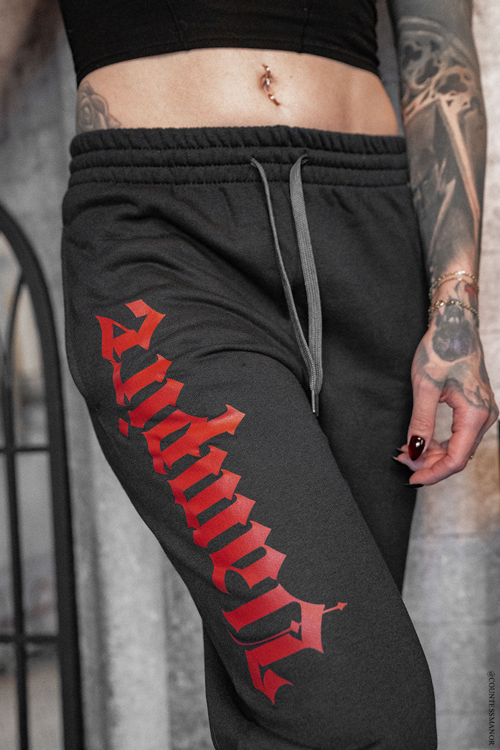 Black sweatpants with red text worn by a person with tattoos.