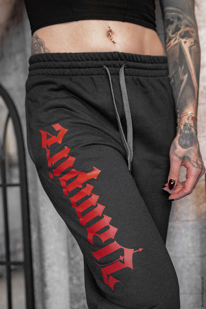 Black sweatpants with red text worn by a person with tattoos.