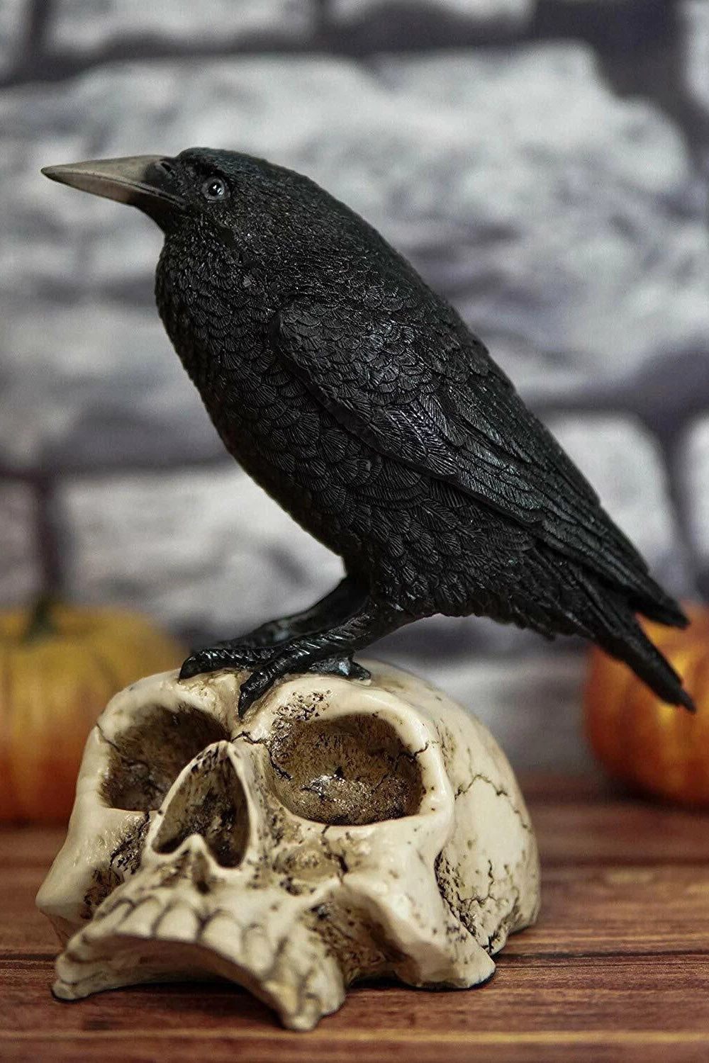 Black crow perched on a skull  statue against a white background by pacific giftware
