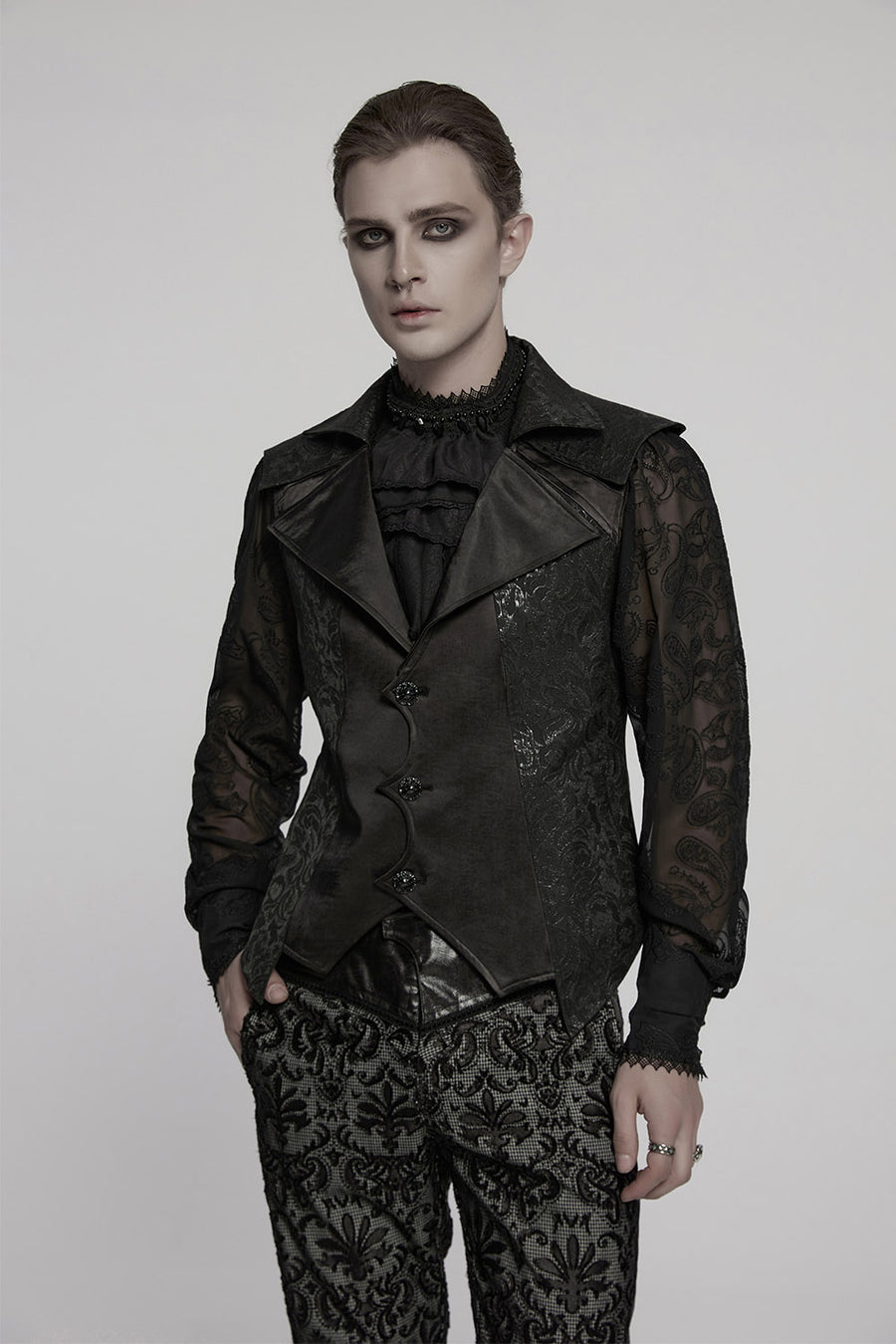 Person wearing a black, ornate outfit with lace details on a plain background