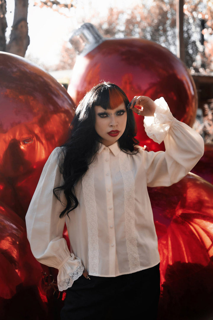 Person wearing a white Victorian vampire inspired button up blouse with large red ornaments in the background