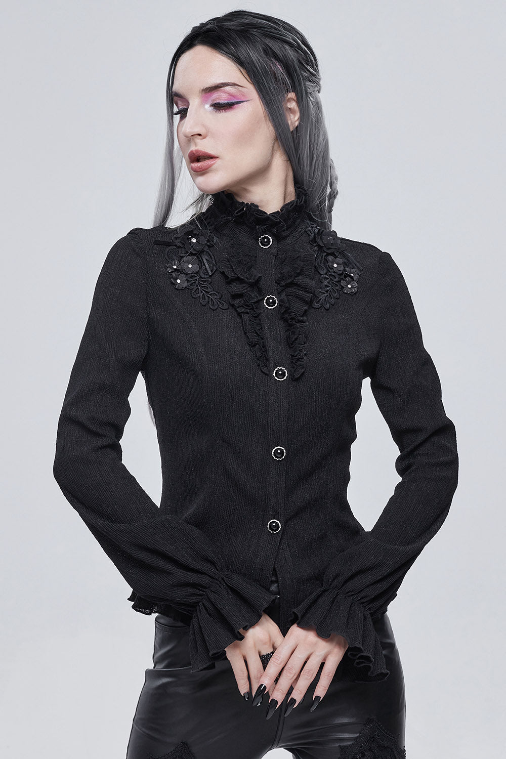 Woman wearing a black gothic-style blouse with ruffled details on a white background