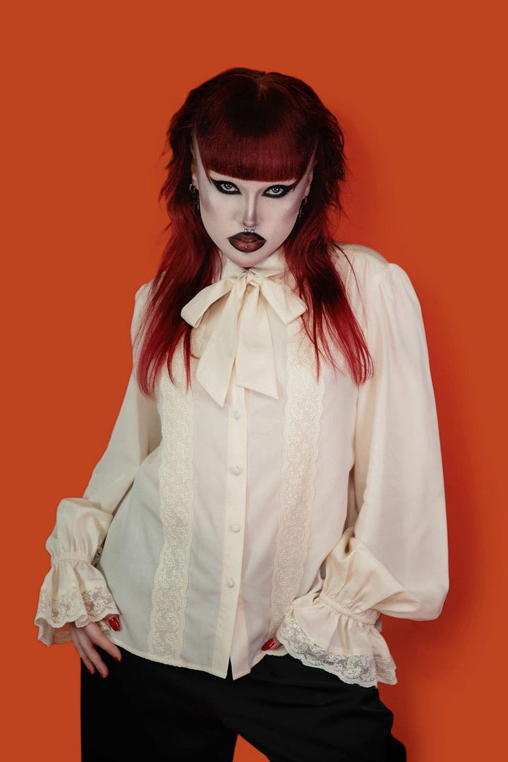 Person wearing a white viscose blouse with a large bow tie against an orange background