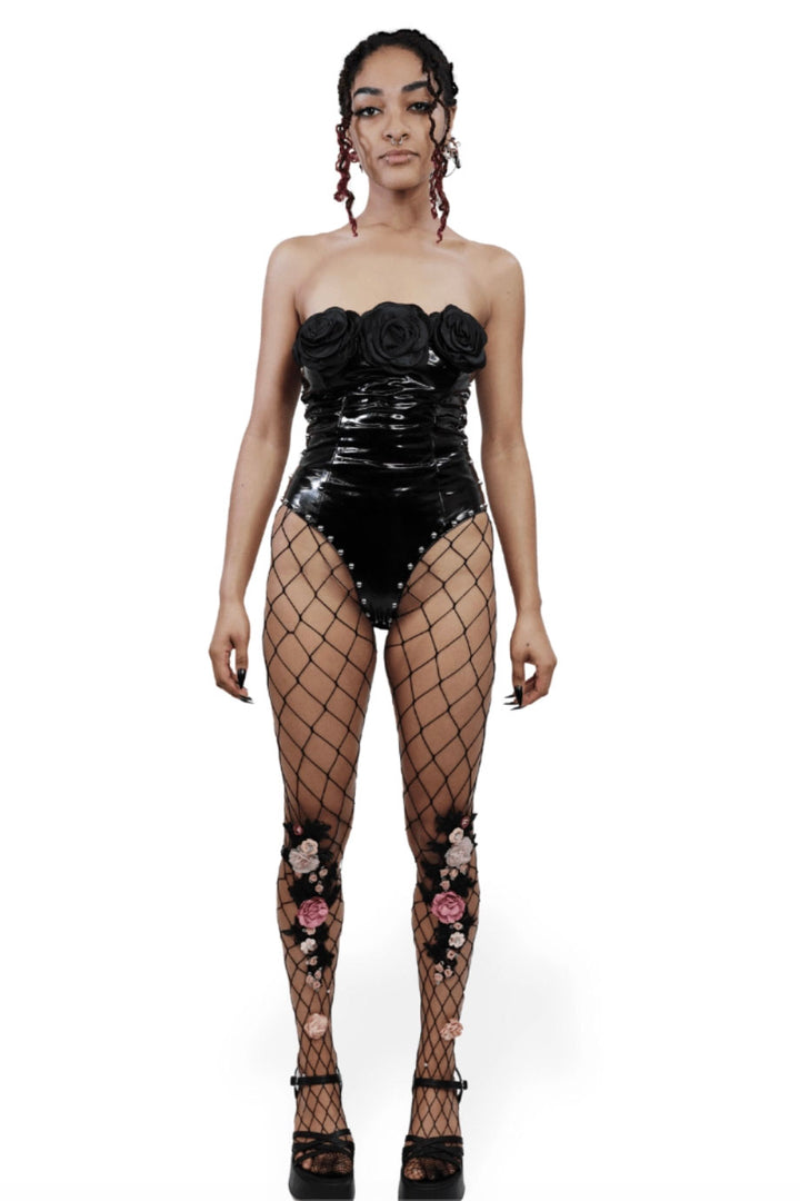 Woman wearing a black floral bodysuit and fishnet stockings on a white background