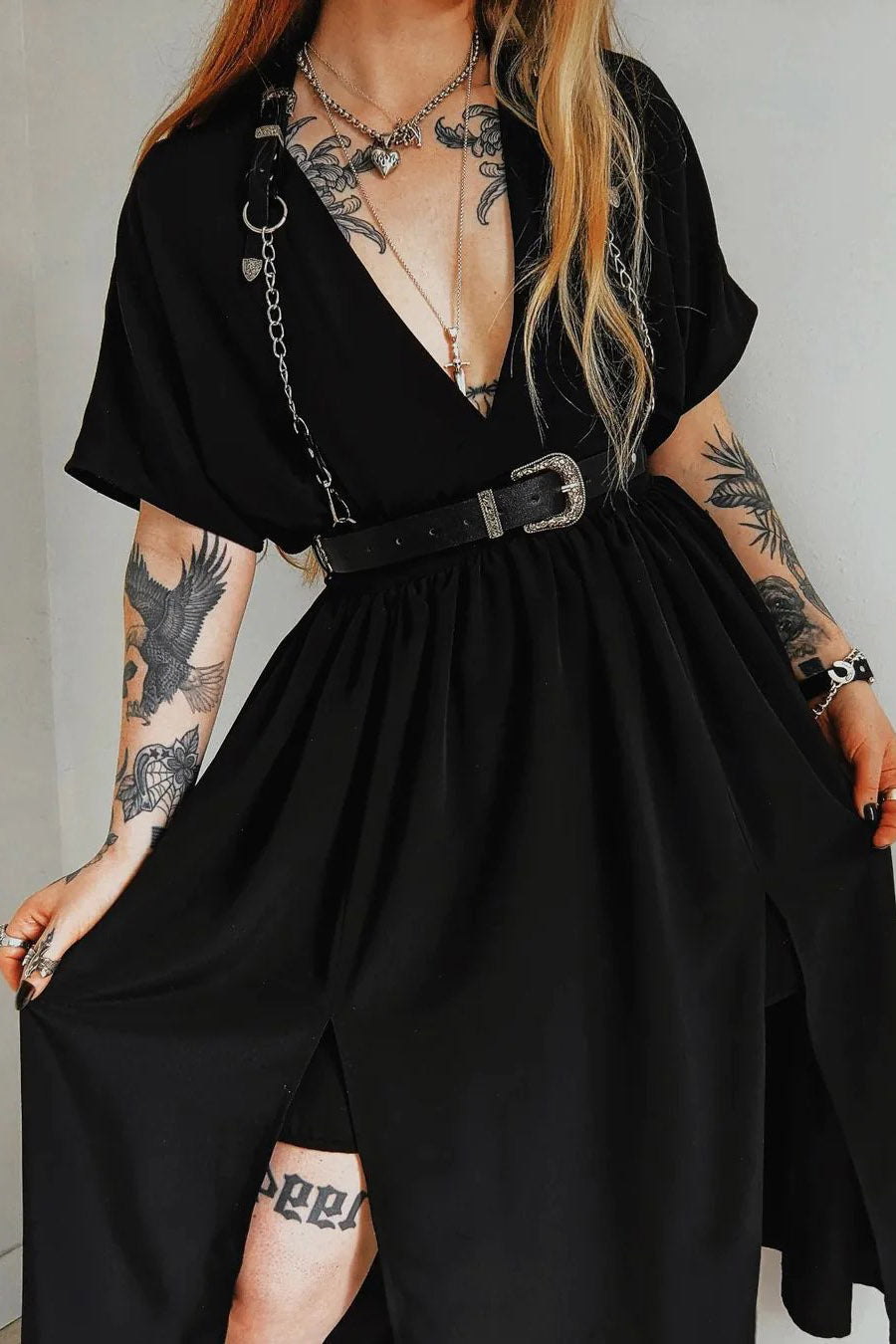 A person wearing a black gothic harness belt with silver chains and western buckles, featuring adjustable shoulder straps and a waist belt.