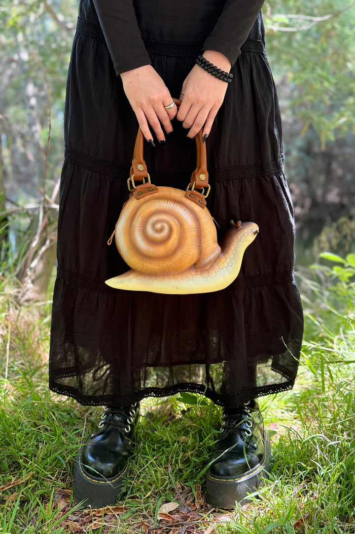 Person holding a snail-shaped handbag in a natural setting