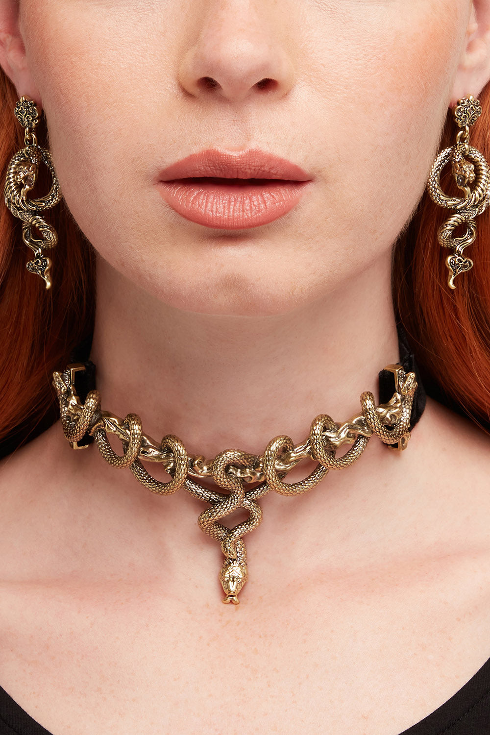 Gold snake necklace and earrings on a person with red hair.