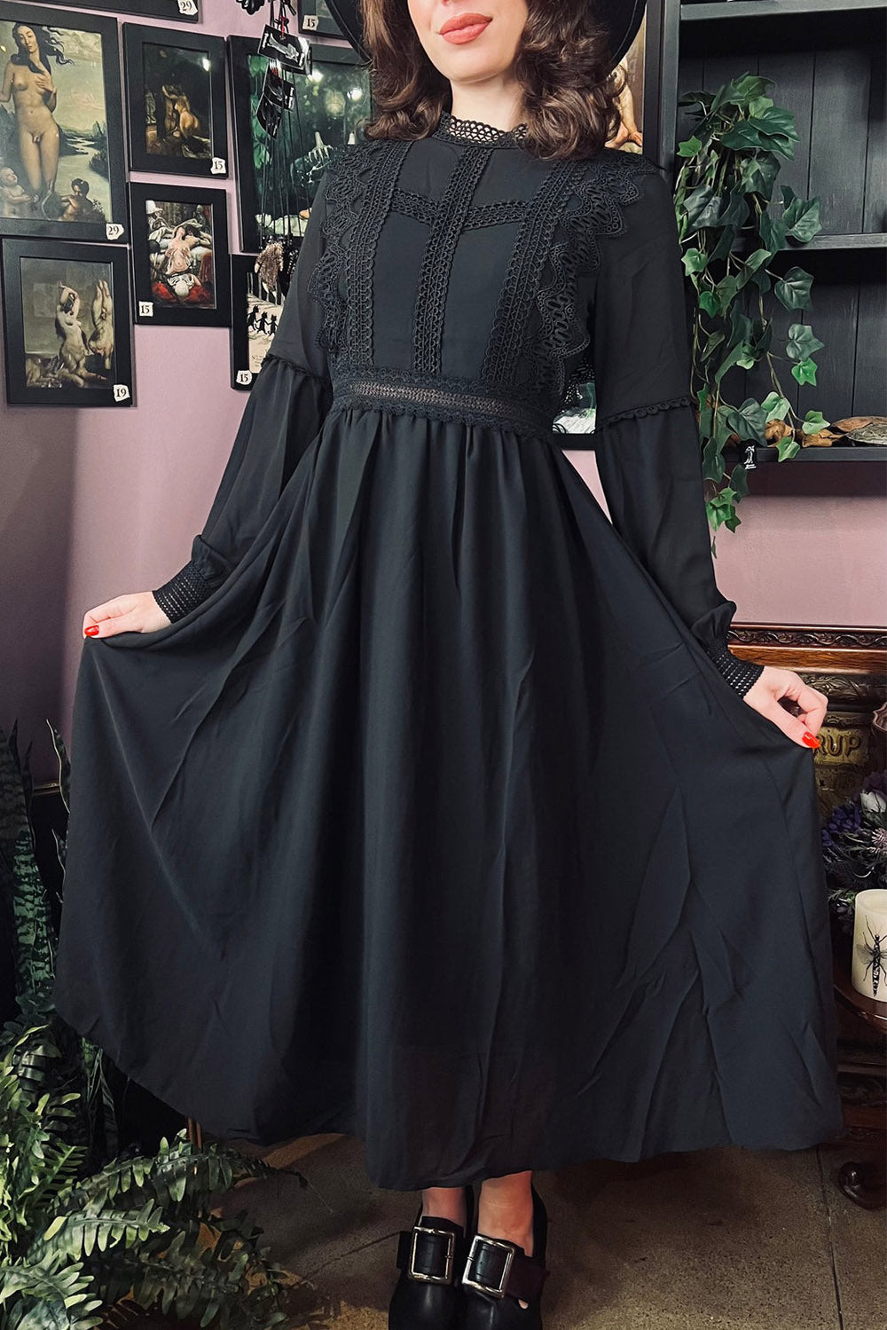 Woman wearing a midi length black dress by witchwood bags standing in a room with framed pictures on the wall.