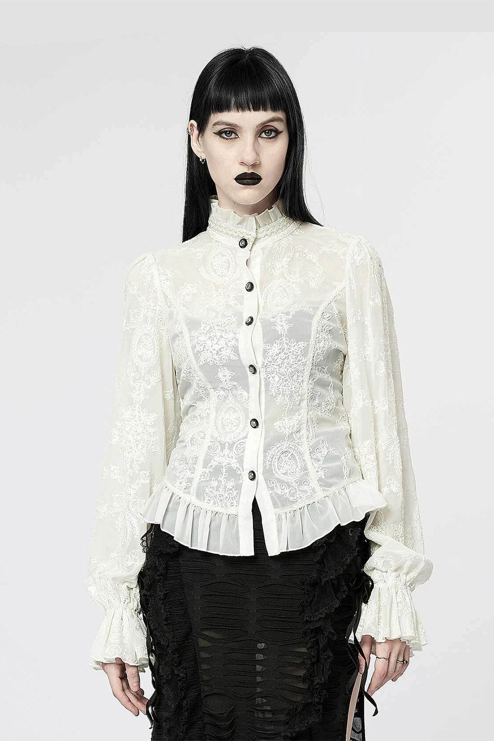 Person wearing a white lace blouse with black buttons on a white background