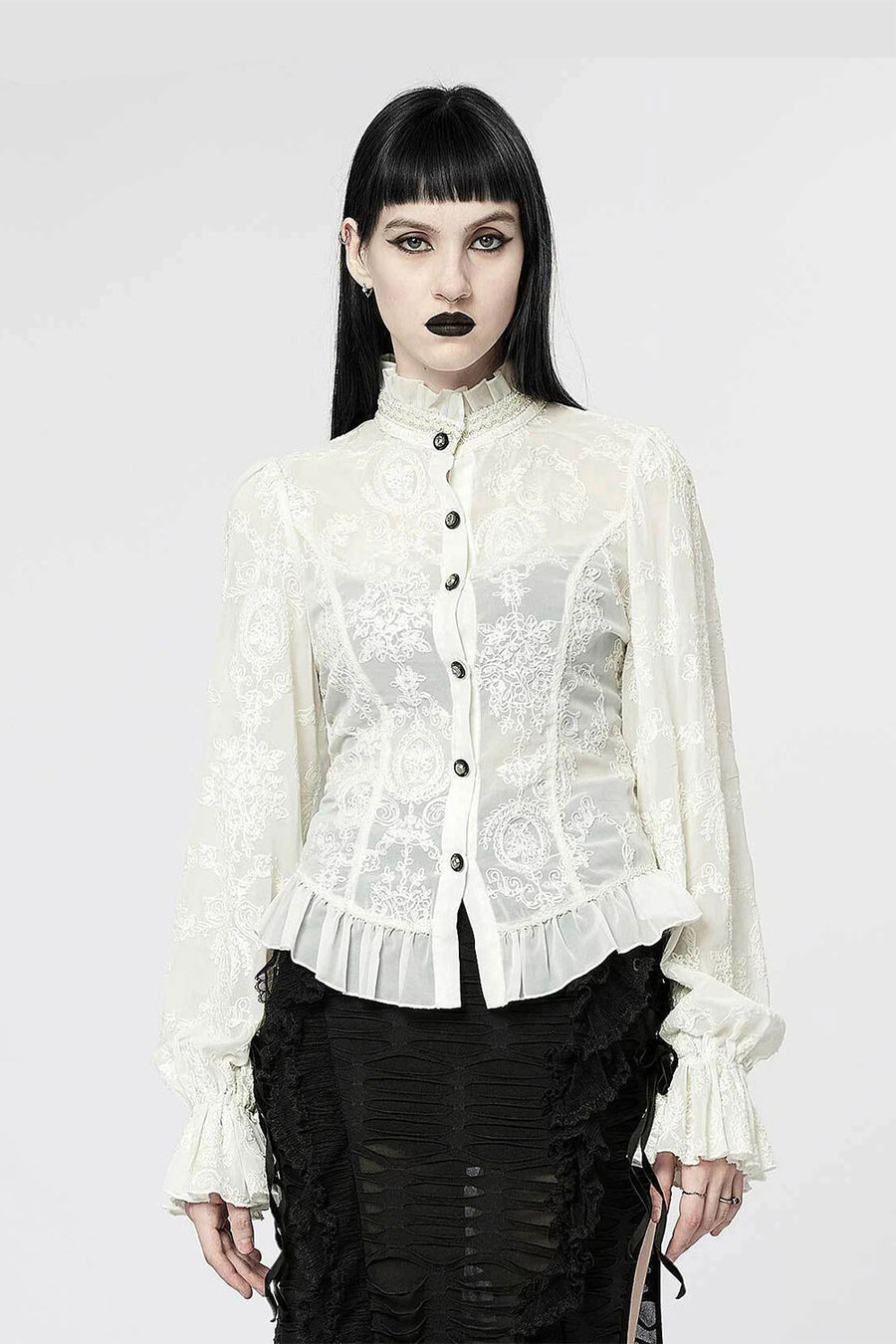 Person wearing a white lace blouse with black buttons on a white background